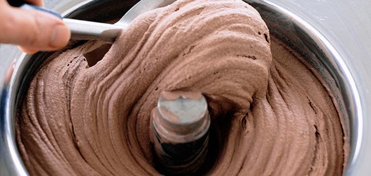 Mano batiendo helado de chocolate en recipiente de aluminio
