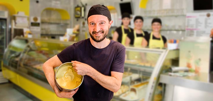 hombre sosteniendo recipiente con helado frente vitrina refrigerada y personas