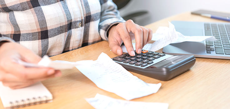 Persona realizando cuentas en una mesa con calculadora y recibo en mano