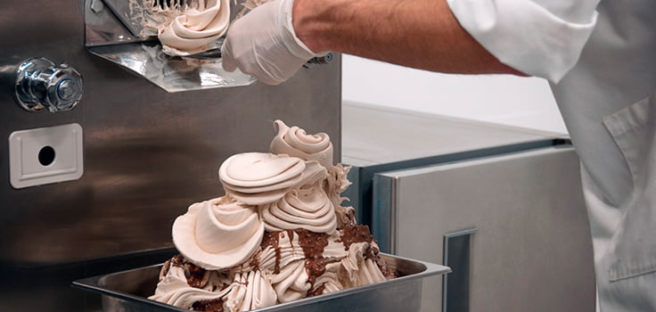 Persona sirviendo helado de la maquina a recipiente de aluminio
