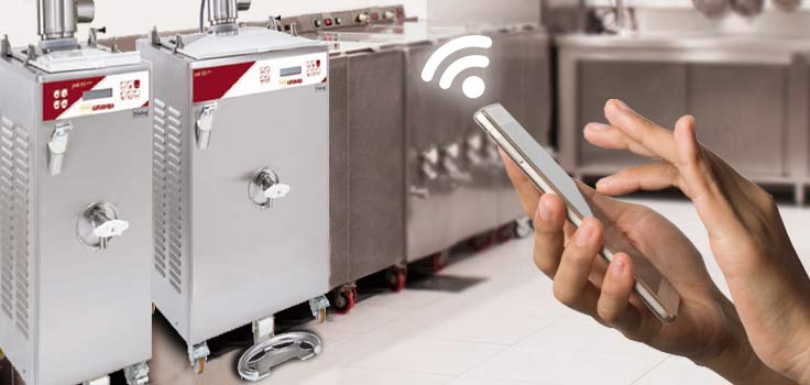 Persona sujetando celular en frente a dos máquinas pasteurizadoras para helados representando el manejo remoto